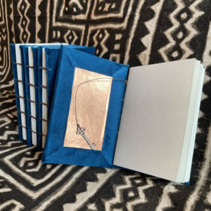 This is an image of handmade sketchbooks. This particular image features one book laying open to show the metallic interior and key shaped bookmark